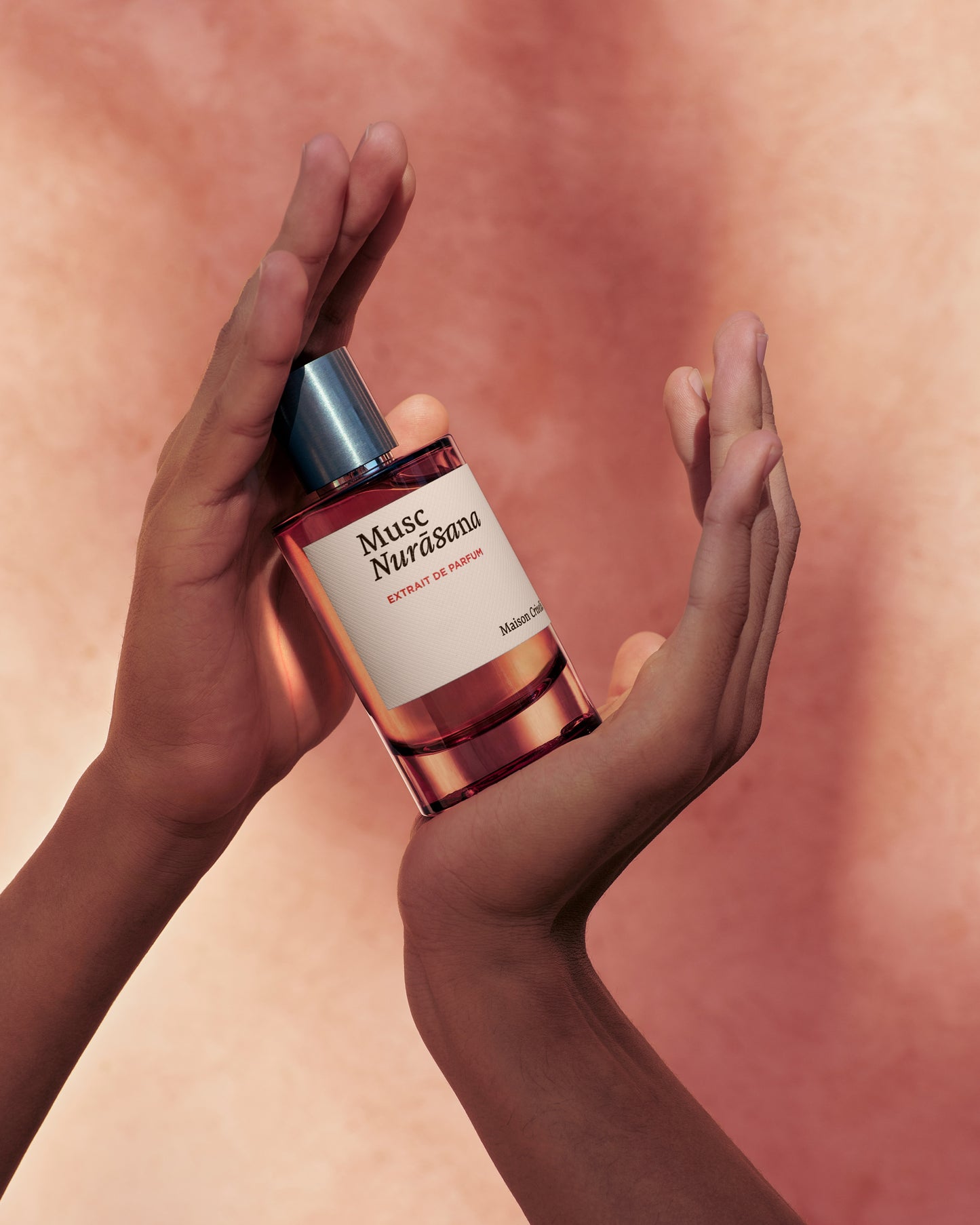 Musc Nurasana perfume bottle held by hands against a peach background