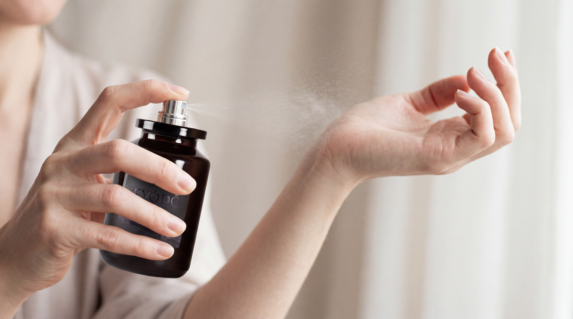 Person applying Kyodo perfume to their wrist with a neutral background